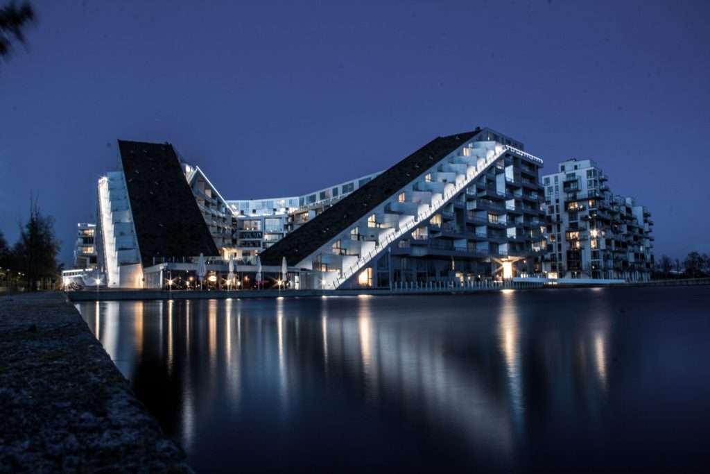Architektonische Nachtaufnahme des 8 House in Kopenhagen mit Lichtspuren und Wasserreflexionen.